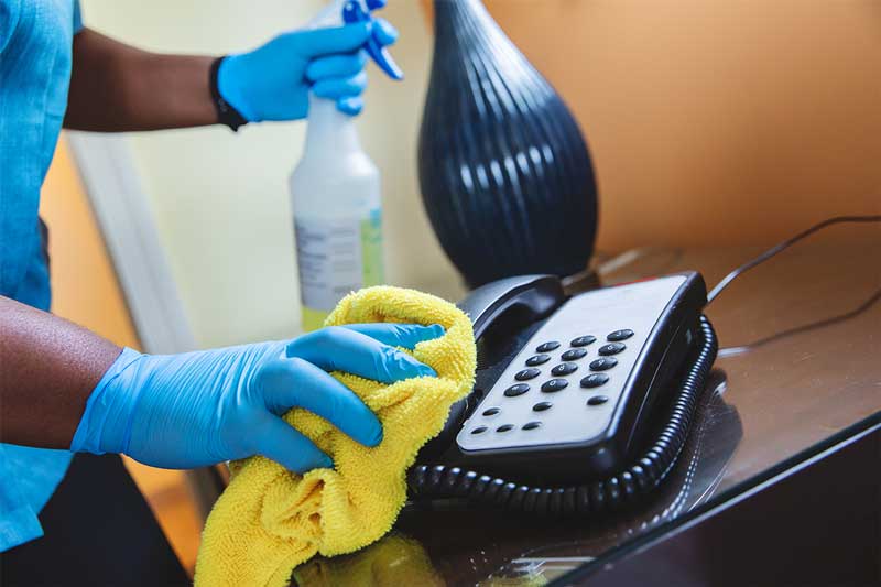 Persona con un aerosol y un paño amarillo limpiando un teléfono en el resort